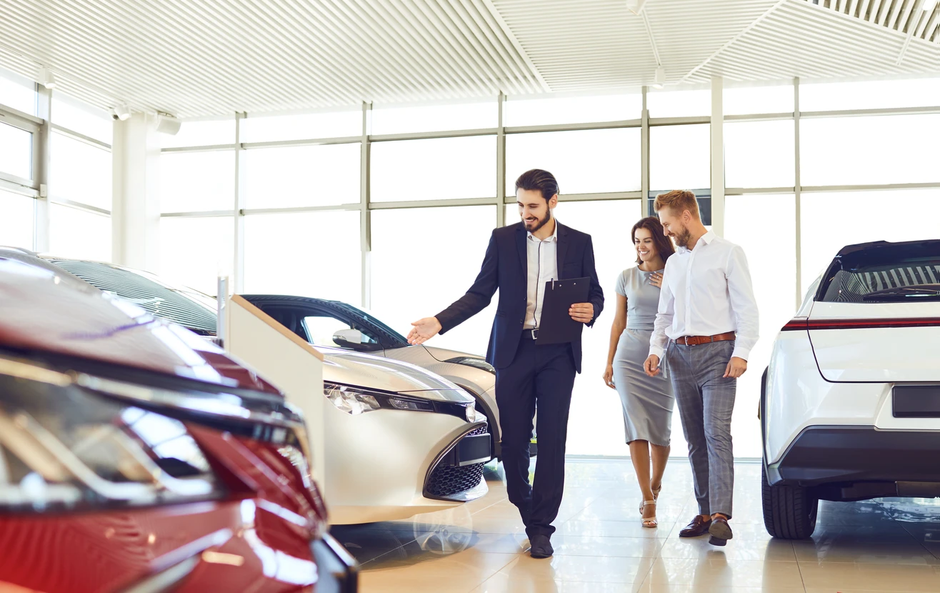 Showroom automobile moderne avec vendeur en costume présentant véhicules à couple de clients