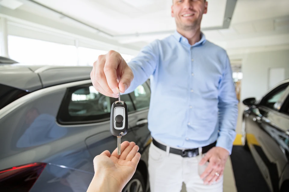 Un homme en chemise bleue remet les clés d'un véhicule à un client dans un garage automobile