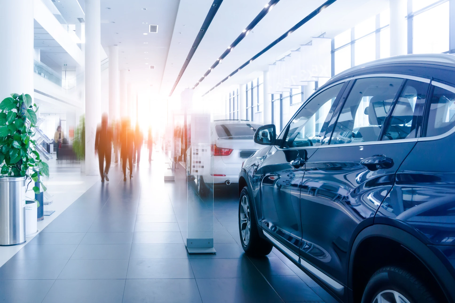 Showroom automobile moderne avec véhicules SUV exposés, visiteurs flous en mouvement dans un espace lumineux aux lignes contemporaines