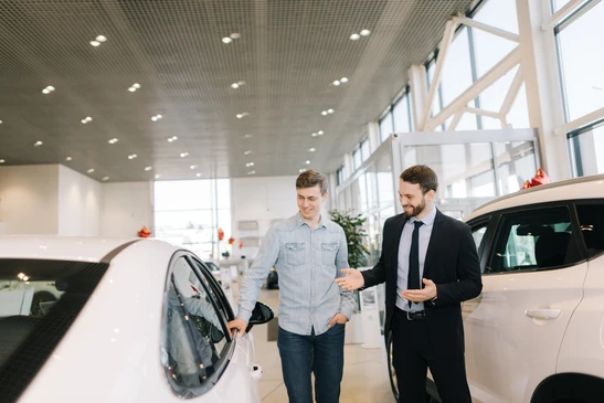 Concession automobile moderne avec vendeur en costume pr&eacute;sentant v&eacute;hicules neufs &agrave; client potentiel