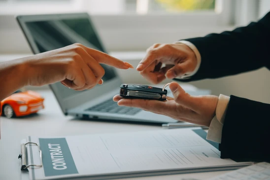 Sc&egrave;ne d'int&eacute;rieur professionnel o&ugrave; deux personnes en costume &eacute;changent des cl&eacute;s de voiture au-dessus d'un bureau