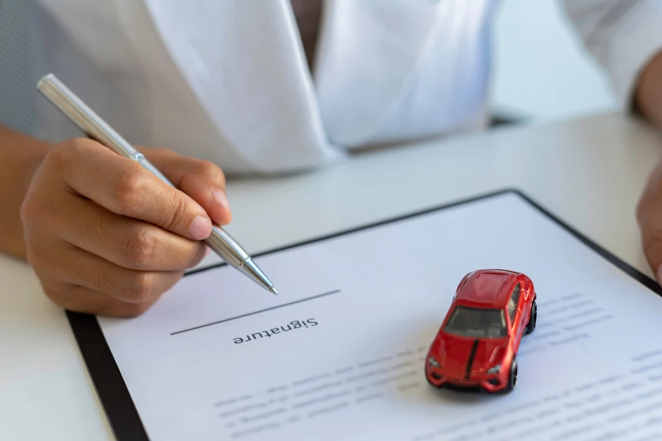 Couple souriant assis face à un conseiller dans un showroom automobile, examinant des documents contractuels sur une table en bois