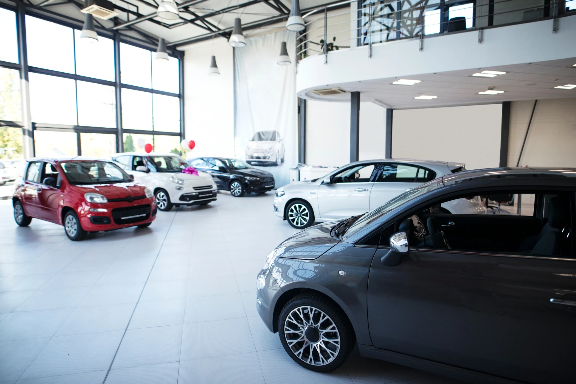 Showroom automobile moderne avec plusieurs véhicules neufs exposés sur sol carrelé blanc